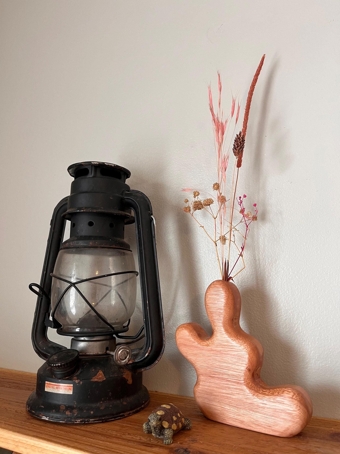 Vintage-style lantern and wooden vase with dried plants on a wooden surface.