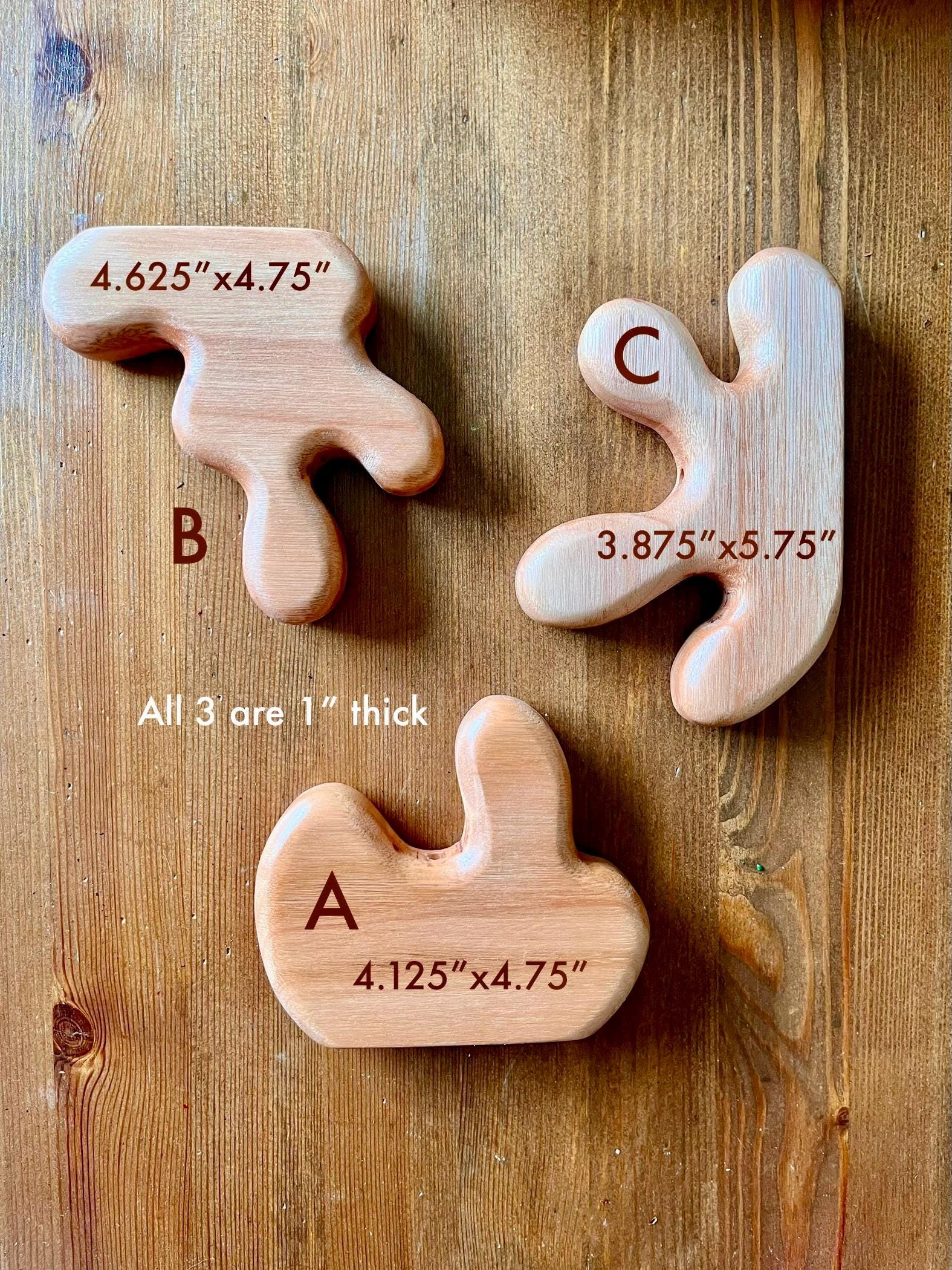 Three wooden letters on a wooden surface with measurements.