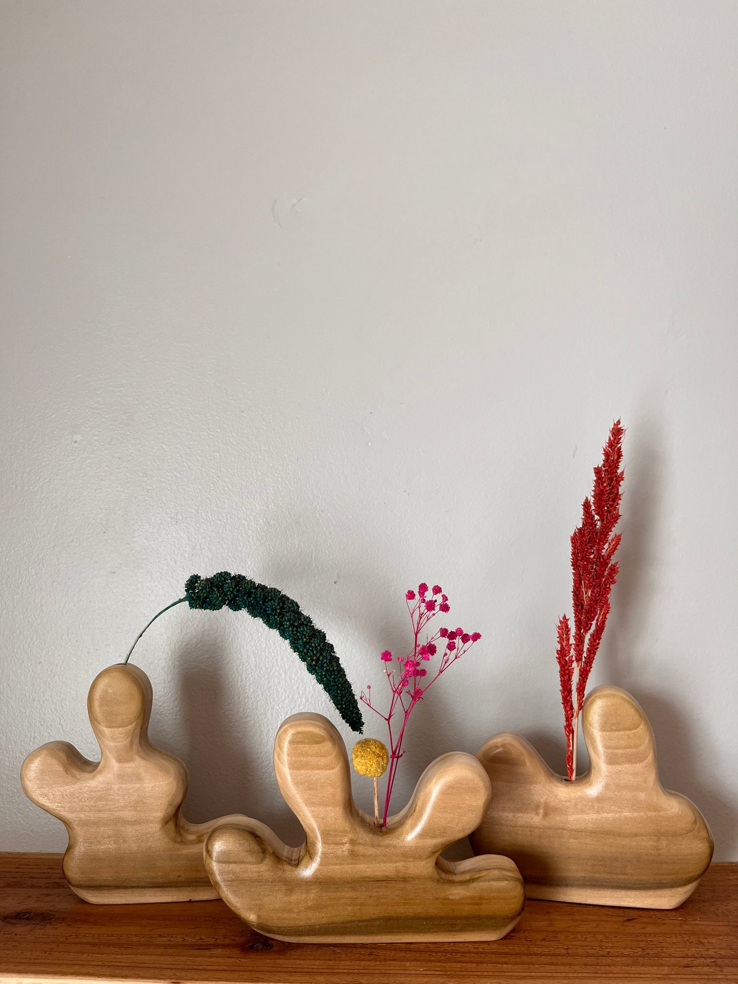 Three wooden vase-shaped sculptures with decorative plants on a wooden surface.